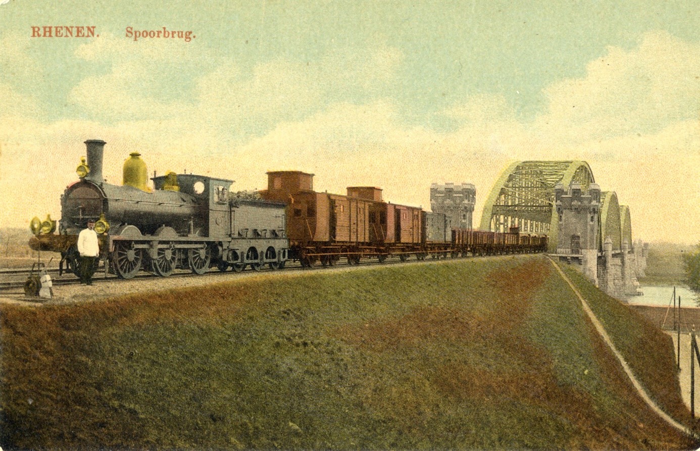 Een goederentrein met locomotief uit de serie 600 HSM rangeert op verkeerd spoor tussen de SM-tramkruising en de brug. Rhenen rond 1920.